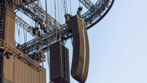 Deux grappes de line array suspendues à la structure d'une scène, vues en contre-plongée