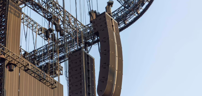 Deux grappes de line array suspendues à la structure d'une scène, vues en contre-plongée