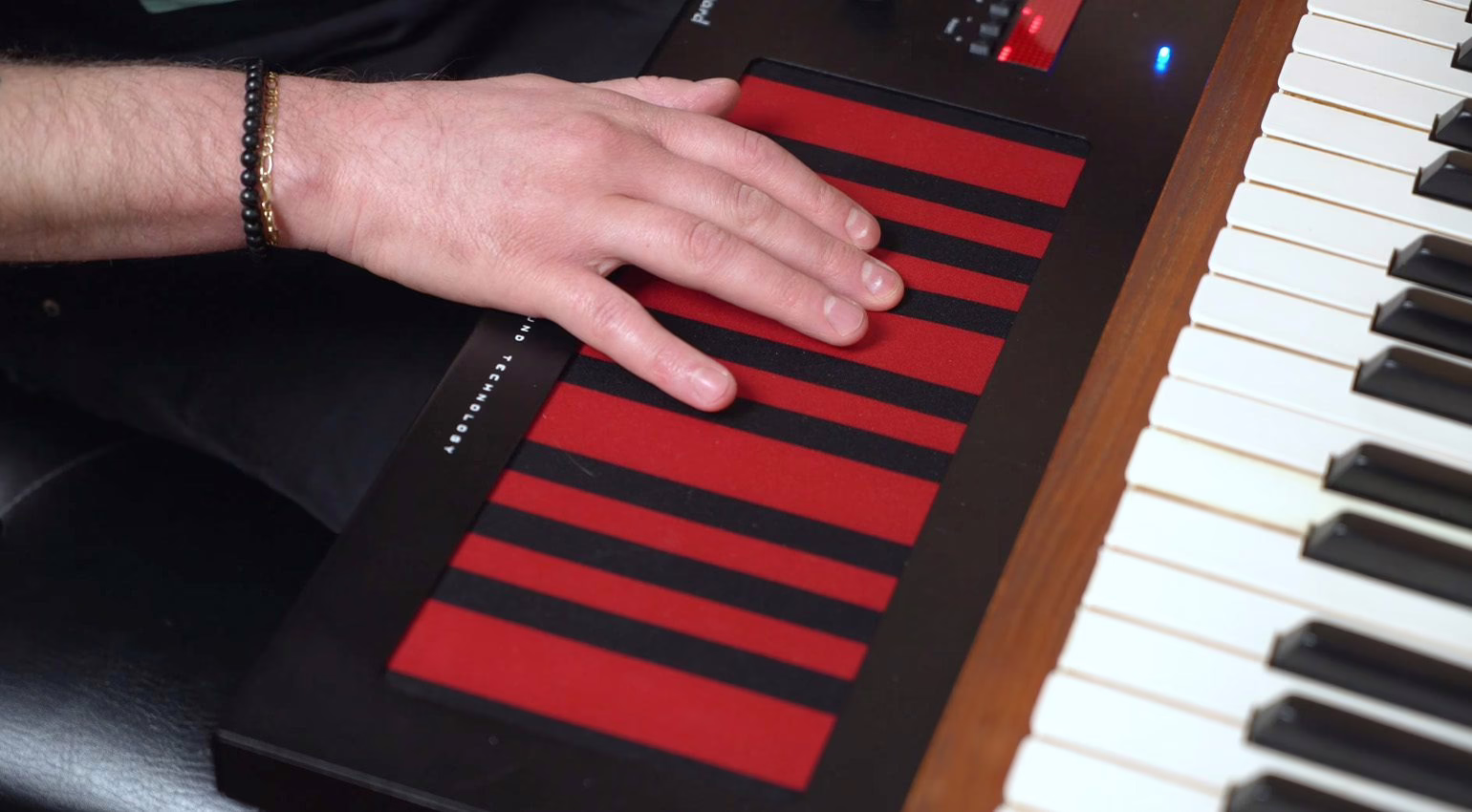 Une main joue sur la surface continue du Haken Slim 21 pose a cote d'un clavier