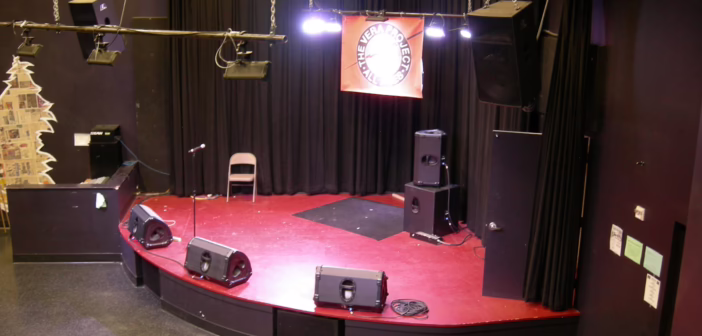 Trois retours de scène alignés au bord du plateau d'une petite salle de concert, avec la diffusion suspendue