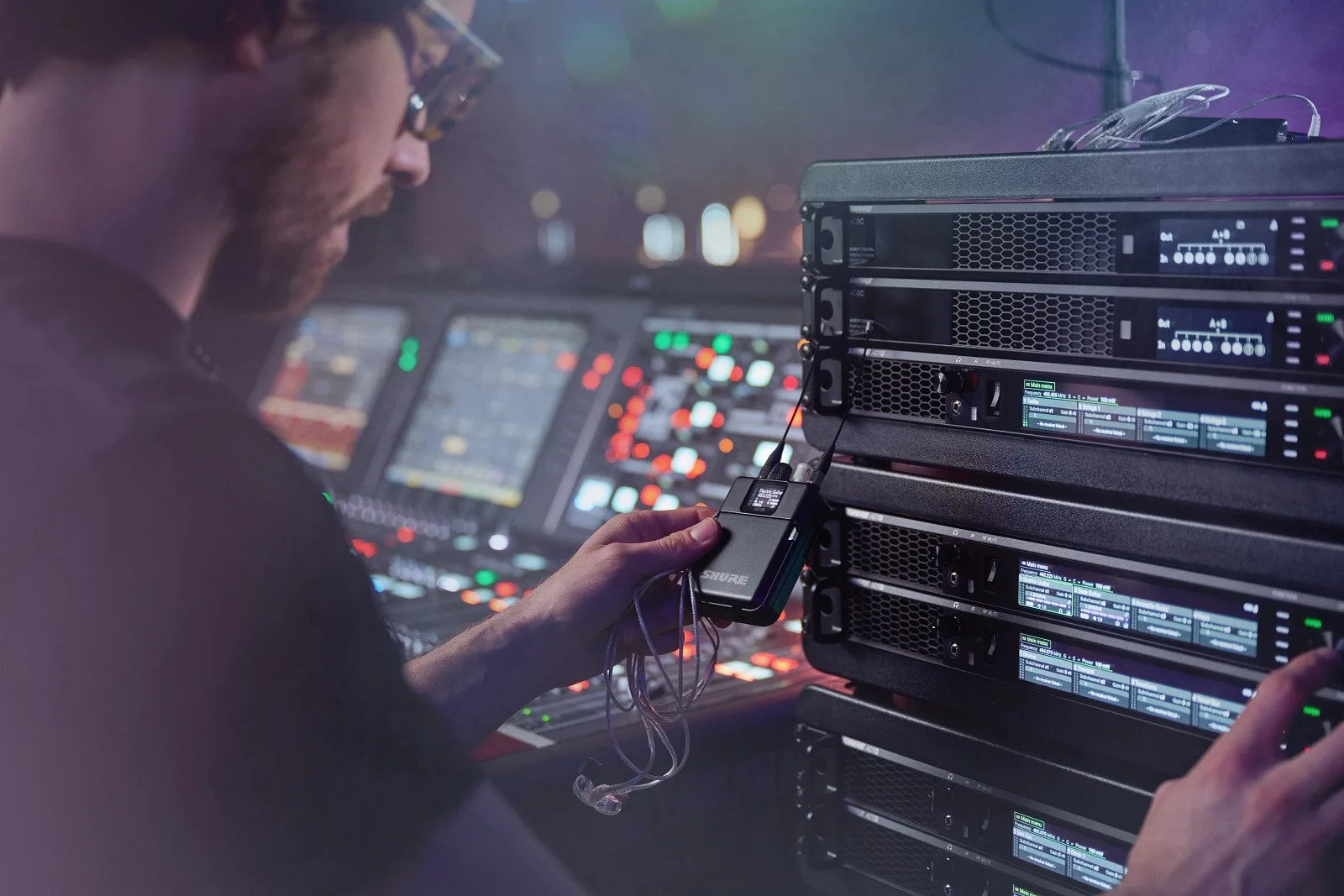 Technicien gérant un système HF Shure Axient Digital en régie, face à un rack de récepteurs